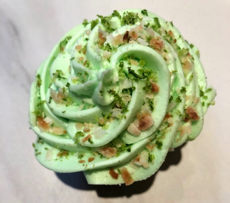 the top of a coconut margarita cupcake with toasted coconut and lime zest on top of the frosting