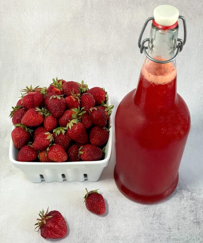 strawberry shrub in a flip top bottle next to fresh strawberries