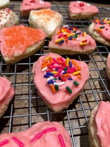 super soft sugar cookies cut into heart shapes with pink frosting and sprinkles.