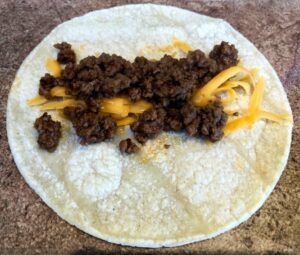 ground beef and cheese on corn tortillas before rolling for taquitos