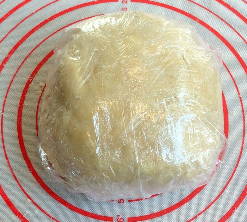 pie crust disc wrapped in plastic wrap on a silicone mat