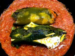 roasted poblano peppers stuffed with cheese in a pan with salsa