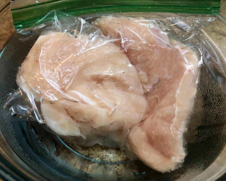 chicken breasts in a plastic bag thawing in a bowl of water