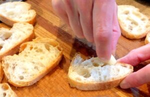garlic slice being rubbed on baguette