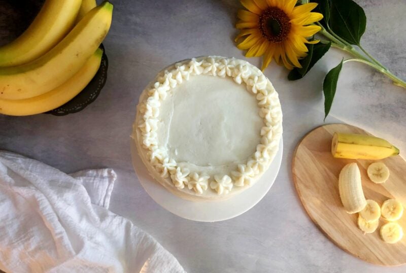 top view of a frosted banana cake with bananas on the side