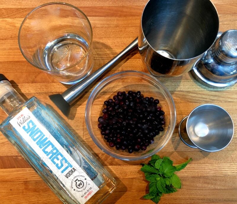 ingredients for a huckleberry cocktail on a wood cutting board