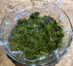 carrot greens pesto in a bowl with plastic wrap on top