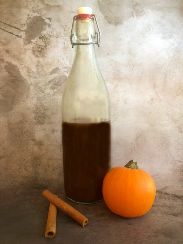 pumpkin spice liqueur in a bottle with cinnamon sticks and a pie pumpkin