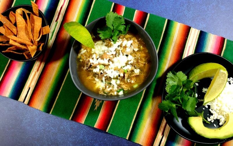 green chicken chile verde with fried tortilla strips, avocado, cilantro and cheese on the side