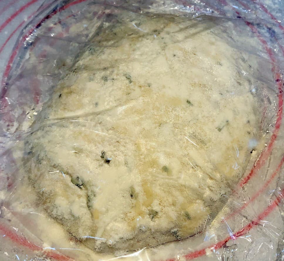 rosemary bread dough in a ball and covered with plastic wrap.
