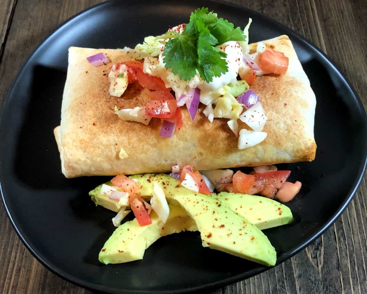 air fryer chimichanga with sour cream, avocado, lettuce, tomato and onion on top.