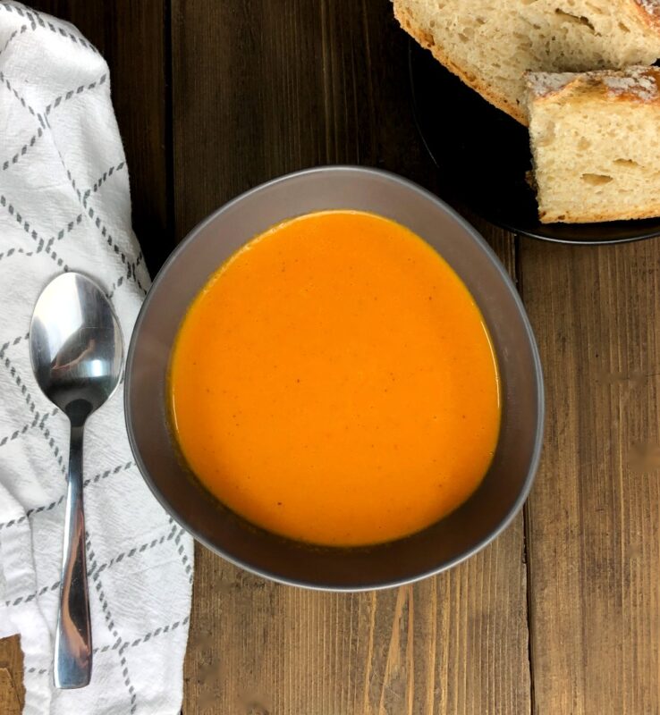 a bowl of orange tomato soup with cream on top bread on the side