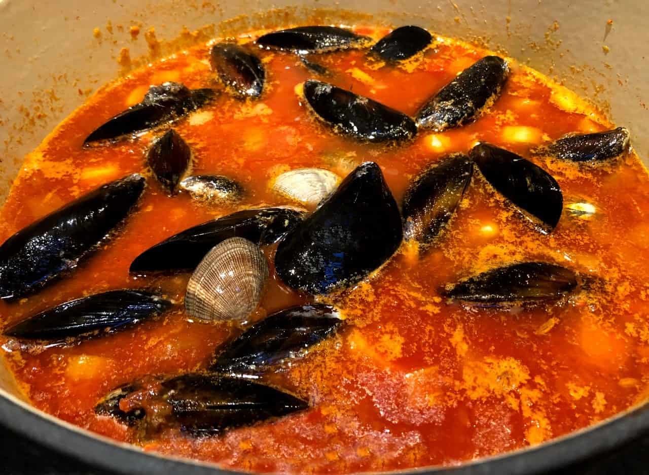 cioppino in a pot with seafood added.
