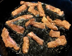 steak pieces frying in a cast-iron pan