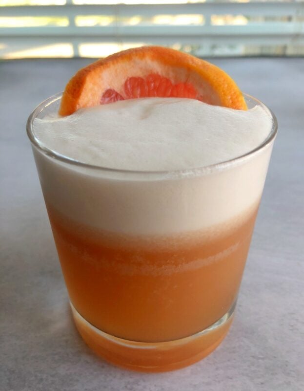 a grapefruit pisco sour in a lowball glass with a slice of grapefruit on top