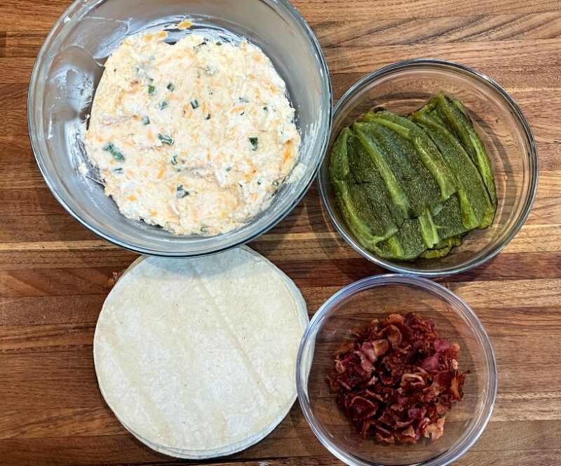 ingredients for jalapeno popper taquitos: cheese mixture, roasted jalapeno halves, bacon, and corn tortillas