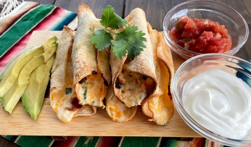 jalapeno popper taquitos with toppings on a wooden board