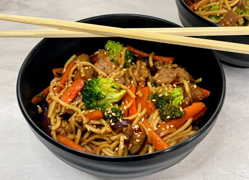 a bowl of udon noodles with beef and vegetables