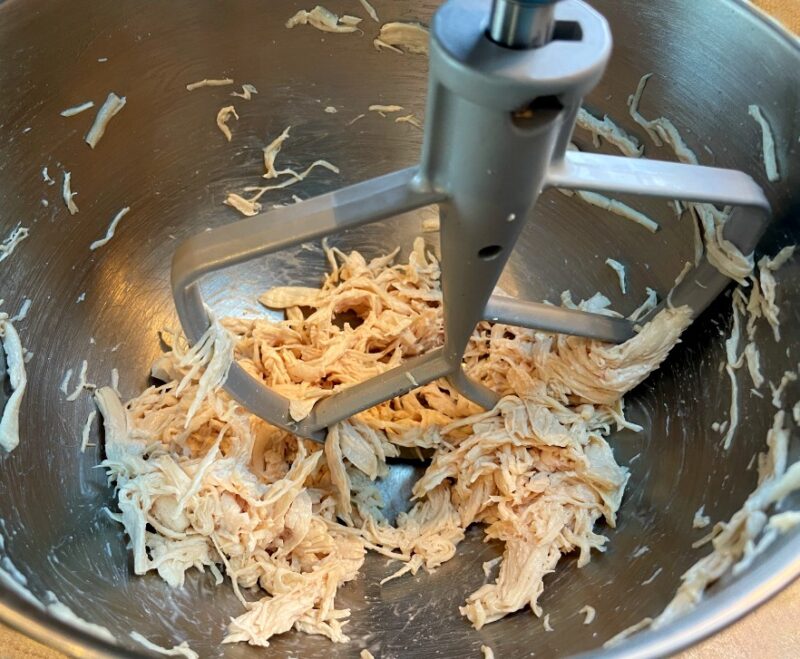 cooked chicken being shredded in a stand mixer