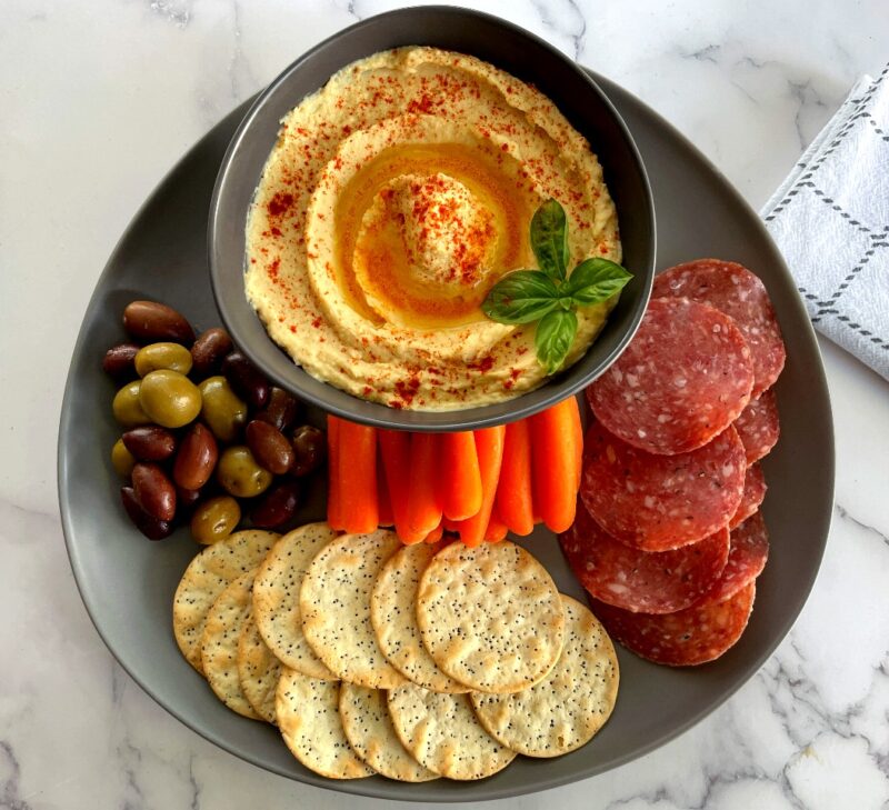 mediterranean hummus plate with salami, crackers, carrots and olives.