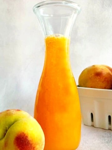 peach syrup in a carafe with fresh peach on the side