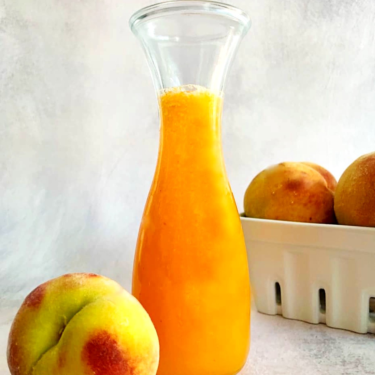 peach syrup in a carafe with fresh peach on the side