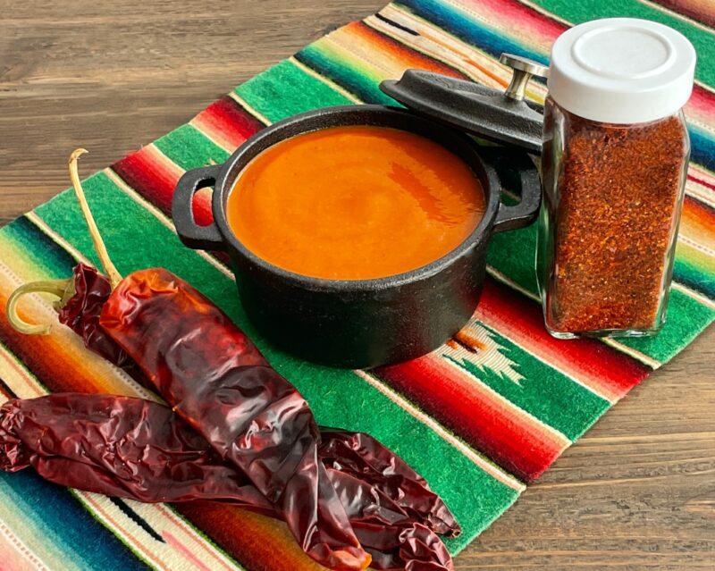 enchilada sauce in a bowl next to dried chiles and dried chile powder