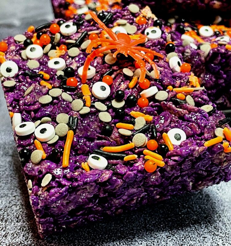 an ube halloween rice krispie treat with eyeball sprinkles and a toy spider on top