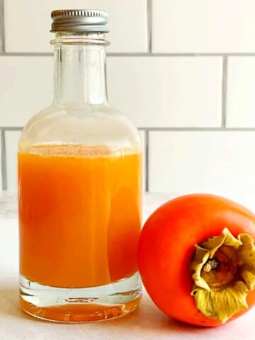 persimmon syrup in a bottle and a fresh persimmon fruit