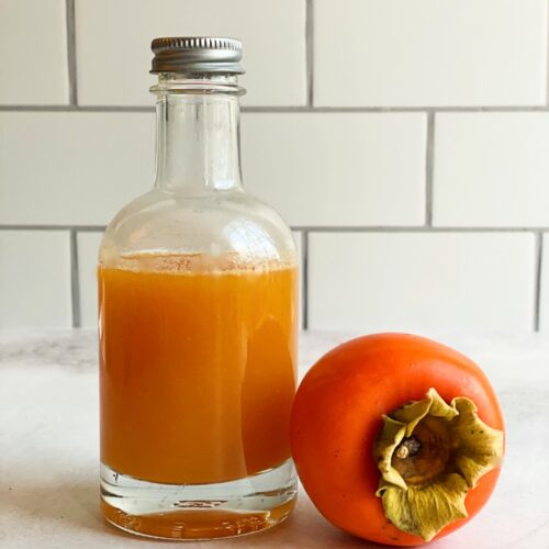 Persimmon syrup in a bottle and a fresh persimmon