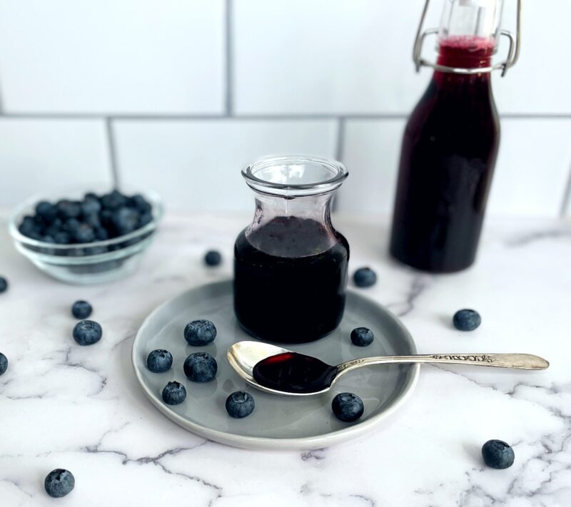 blueberry syrup in a small jar with fresh blueberries on a table