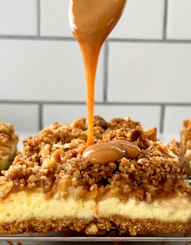 a drizzle of caramel being poured on top of an apple cheesecake bar