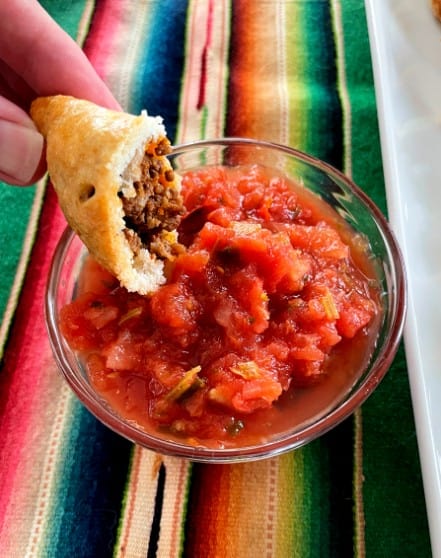 taco hand pie cut in half and dipped in salsa.