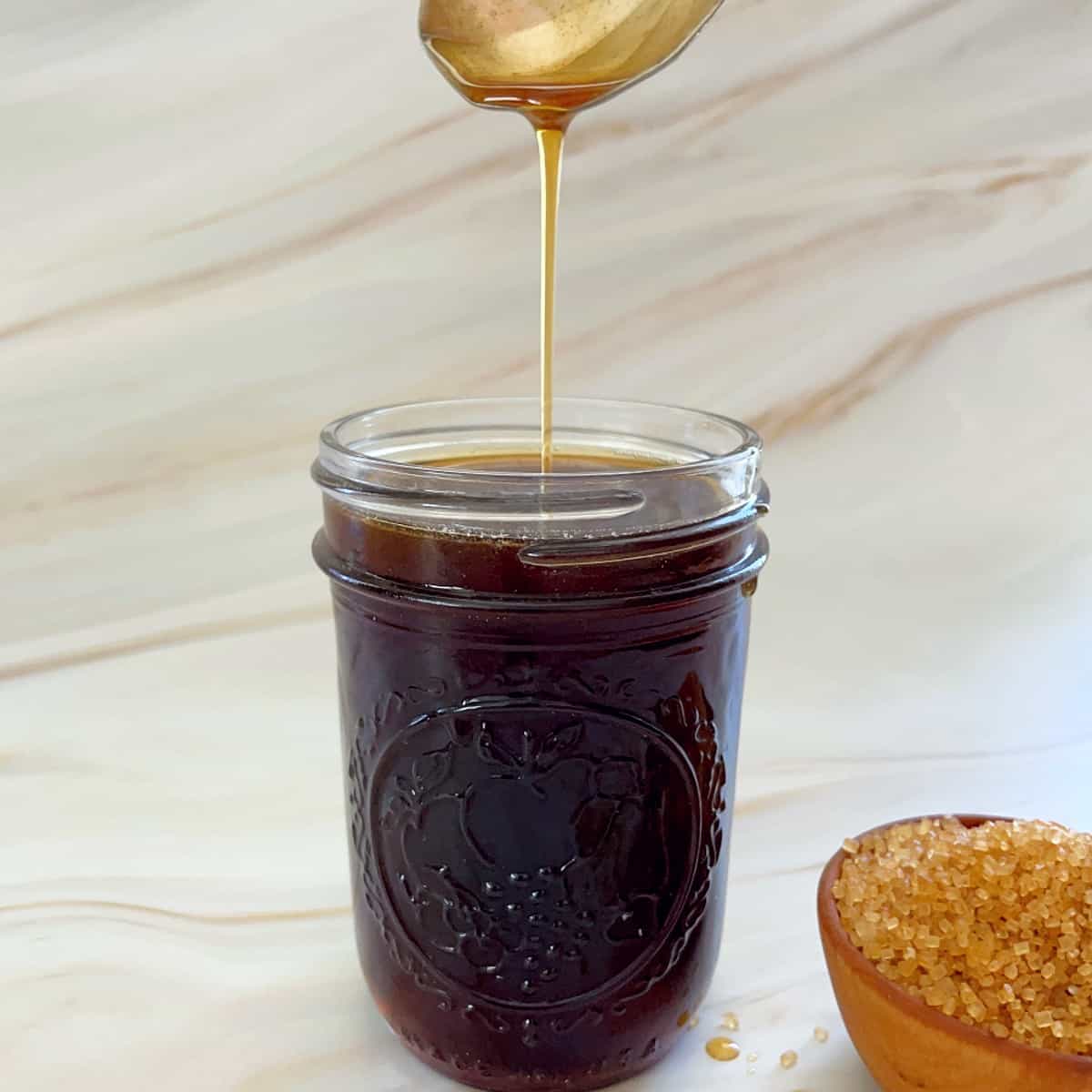 rich demerara syrup dripping off a spoon into a jar.