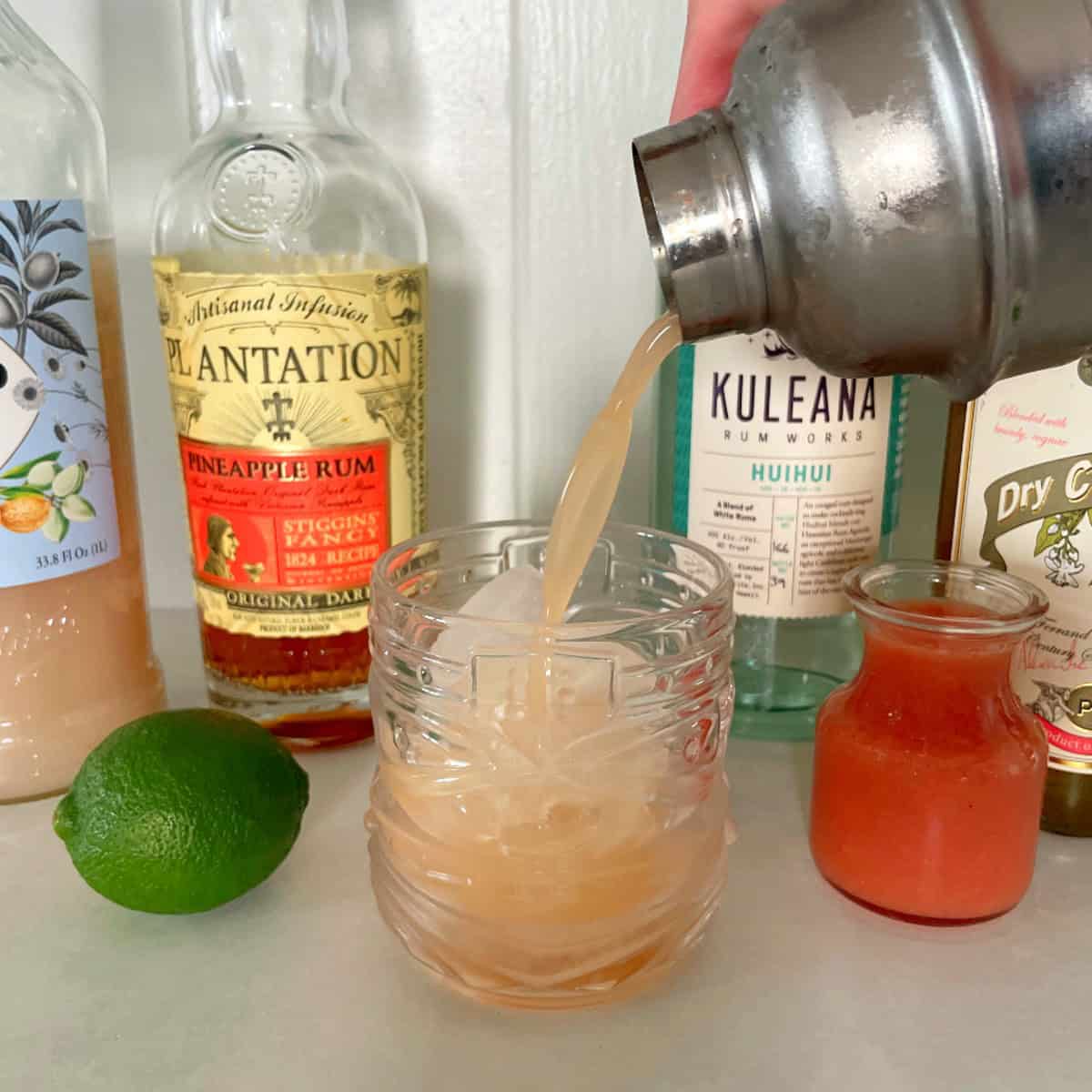 cocktail shaker pouring a guava mai tai into a tiki glass.
