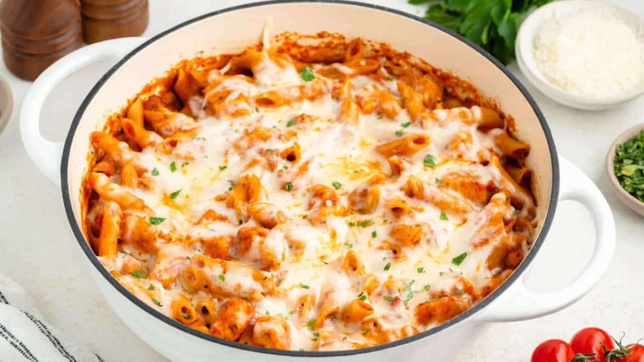 Delicious cheesy baked pasta in a white skillet with herbs and tomato side dishes.