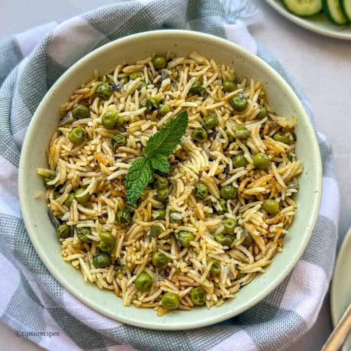 Rice salad with green peas and mint garnished with a mint leaf in a bowl.