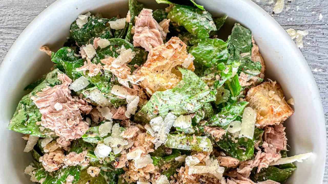 Tuna salad with lettuce, cucumbers, and cheese in a white bowl.